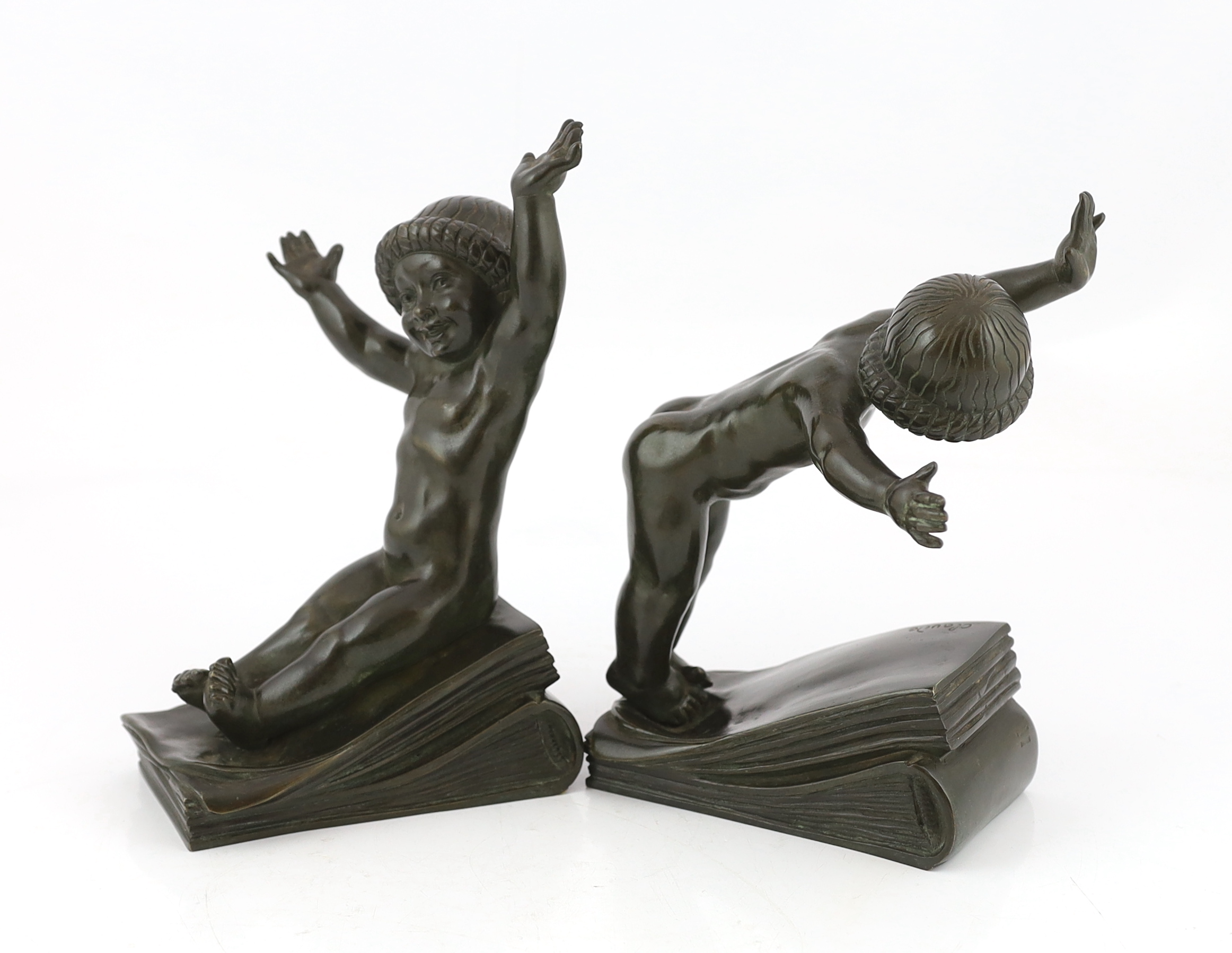 Claude (Claude-Marie Devenet 1851-1931), a pair of French Art Deco bronze bookends, Marcel Guillemard foundry mark, modelled as smiling naked infants standing upon ledgers, signed in the bronze, 16cm wide, 25cm high